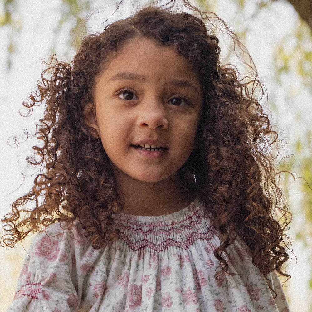 Young girl with curly hair wearing a floral dress outdoors