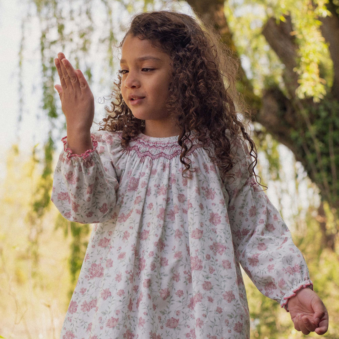 Young girl in a floral dress standing outdoors with trees and flowers in the background