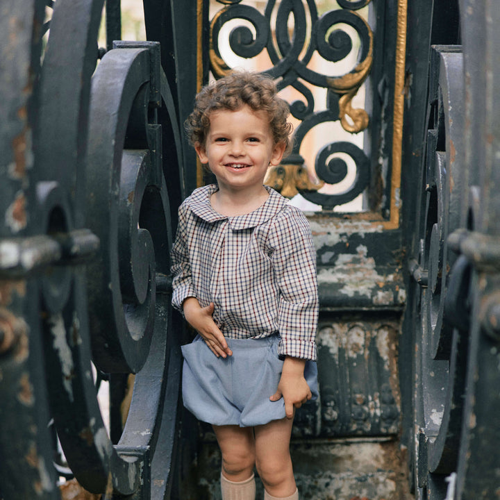 child standing in front of a fence with a tartan shirt