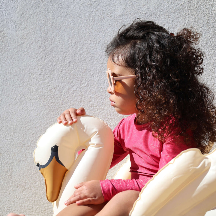 Child sitting on a large inflatable swan float against a light gray wall.