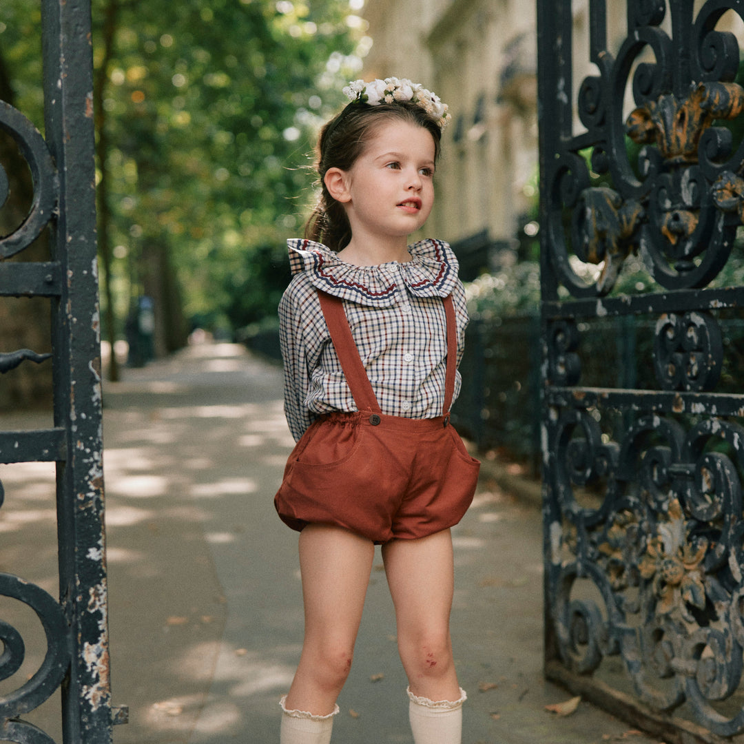 Child in vintage outfit standing in front of an ornate gate