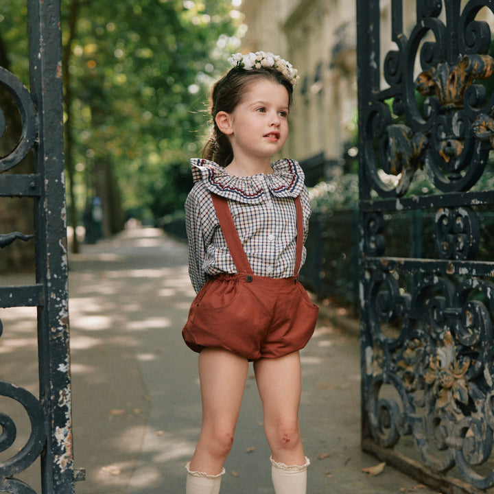 Child in vintage outfit standing in front of an ornate gate