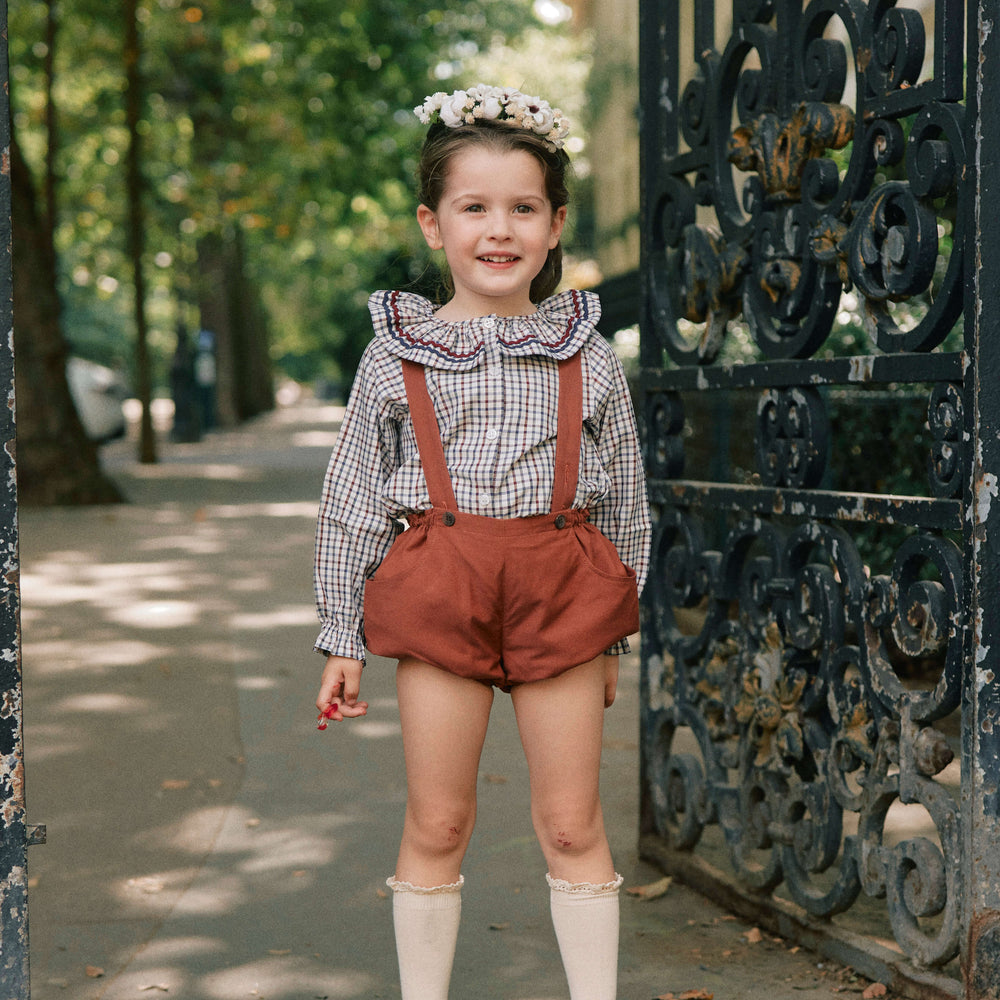Young girl in vintage outfit standing in front of an ornate metal gate.